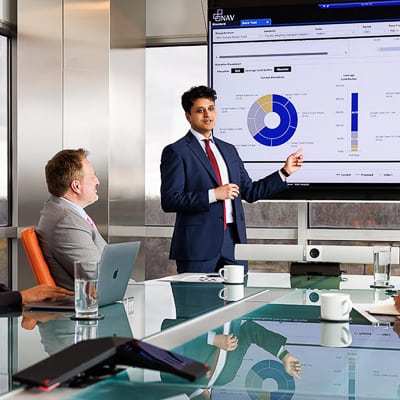 Business presentation in progress with a man pointing at a data chart on a screen while a colleague looks on.
