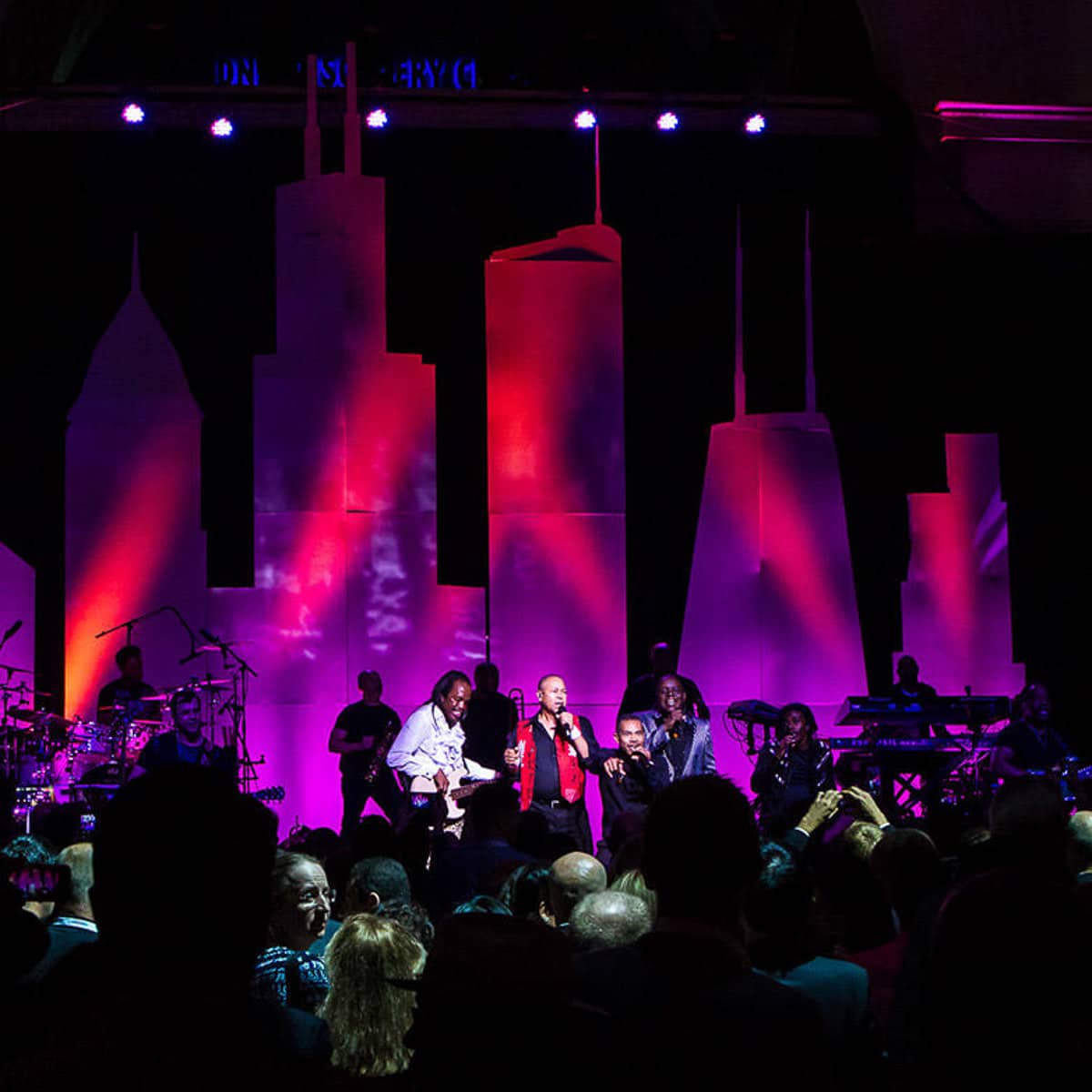 A live band performs on stage during a corporate event with colorful lighting and a full audience